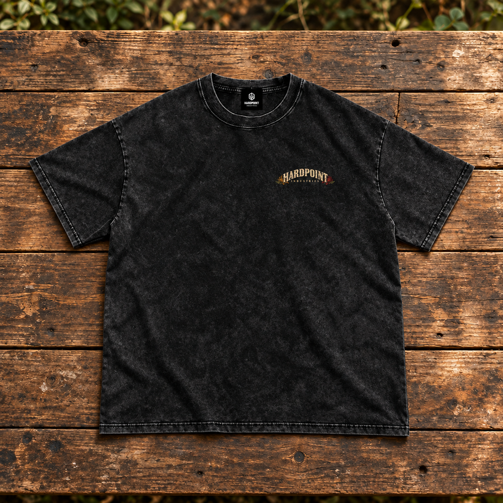 HARDPOINT Mortar Bouquet Snow-Washed Oversized Tee, Black, front view on weathered timber bench. AI-styled product mockup.