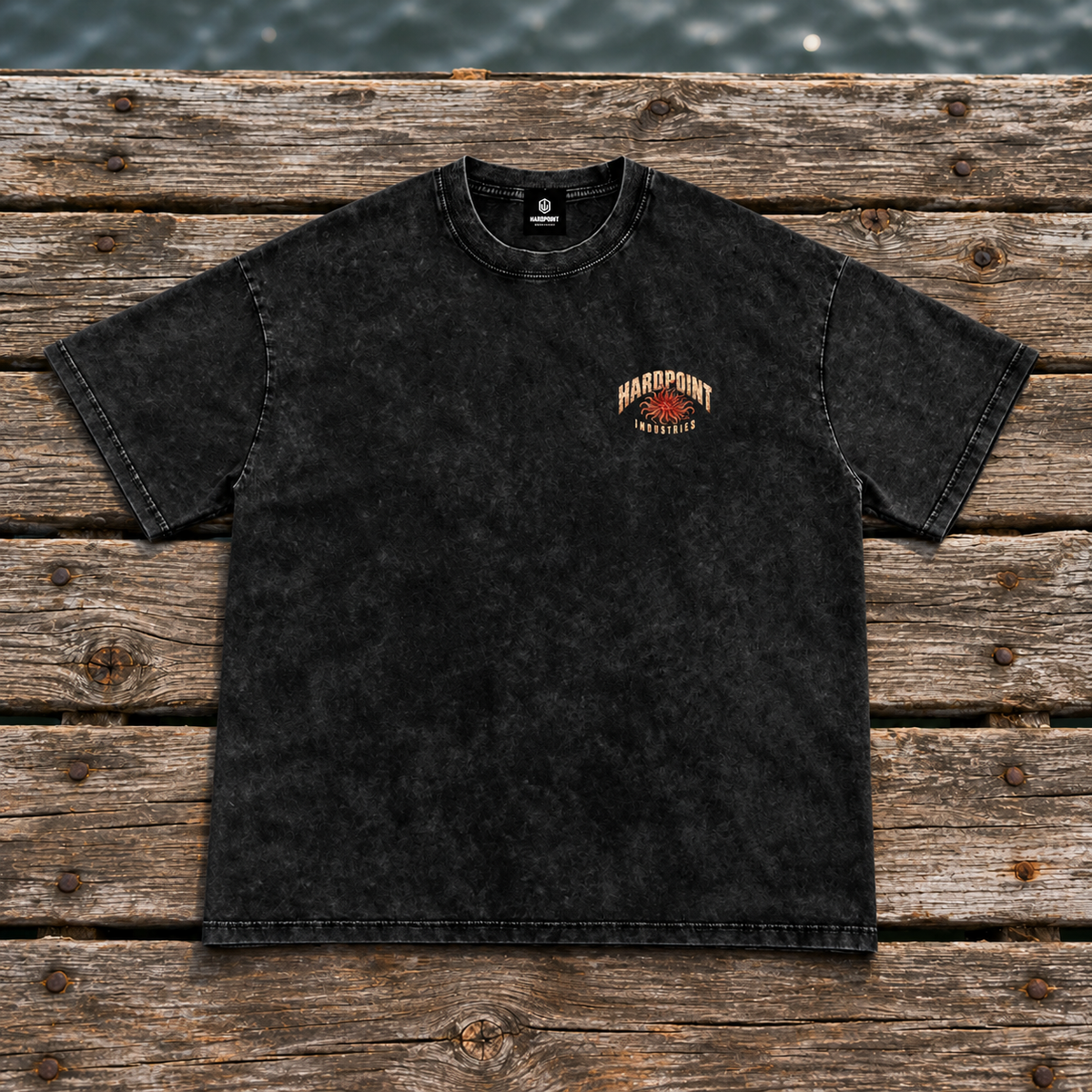 HARDPOINT Tentacle Shell tee, Black, front view on a weathered dock. AI-styled product mockup.